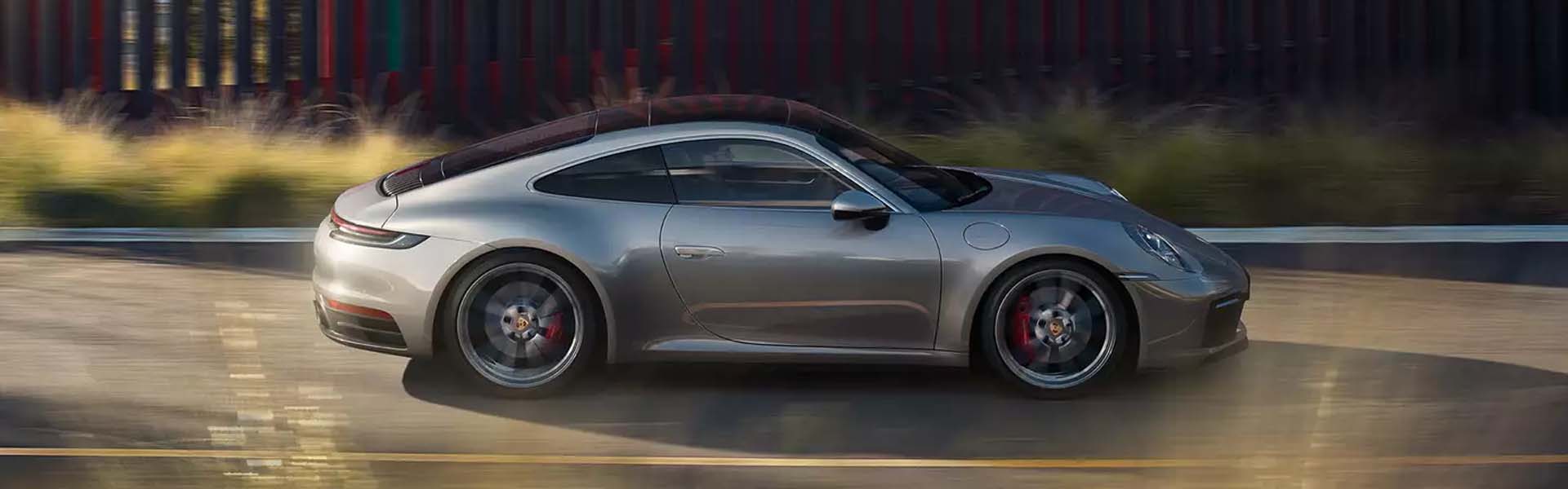 Silver Porsche 911 Targa driving at speed on a road with blurred background foliage.