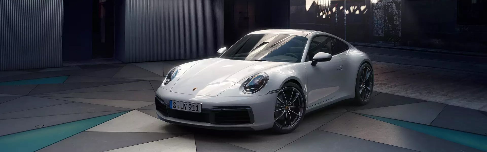 White Porsche 911 parked on a geometric tiled surface with teal accents, under dark lighting.