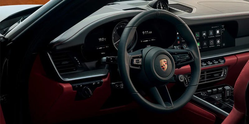Interior of a modern Porsche, featuring a black steering wheel with the Porsche emblem, digital dashboard, and infotainment screen.