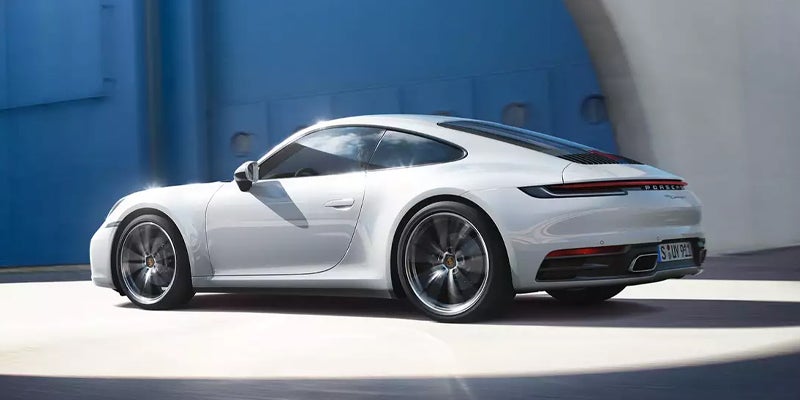 Side-rear view of a white Porsche 911 Carrera 4S driving quickly into a blue tunnel.