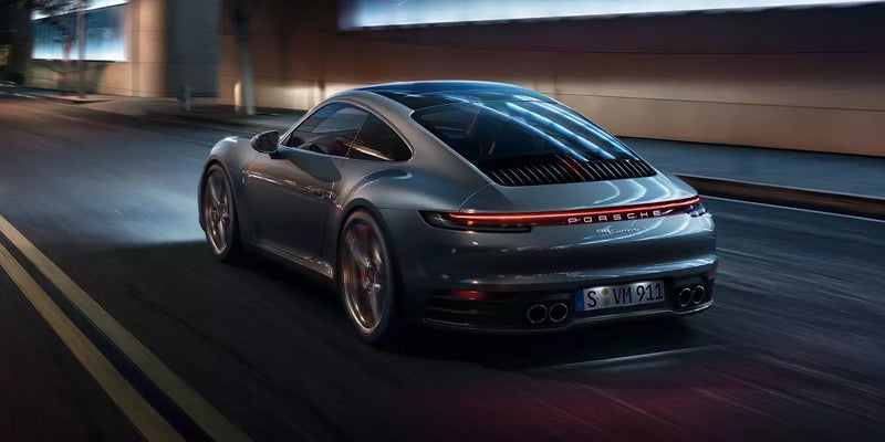 Rear view of a dark grey Porsche Carrera with bright red taillights driving on a dark street at night.