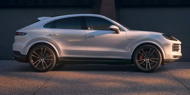 Side view of a white Porsche Cayenne SUV with a sloping roofline, parked on asphalt with warm evening light.