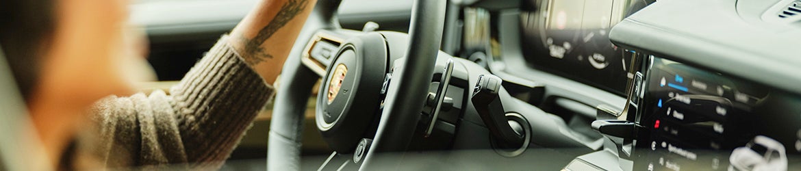 Someone with a tattooed arm in a brown sweater driving a car with a modern dashboard and digital displays.