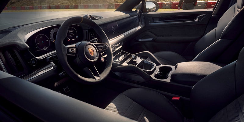 Interior of a luxury car with a black steering wheel, dashboard displays, and leather seats, taken from the passenger seat.