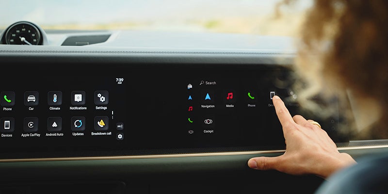A hand interacting with a car's digital dashboard showing app icons like Phone, Car, Climate, and Navigation.