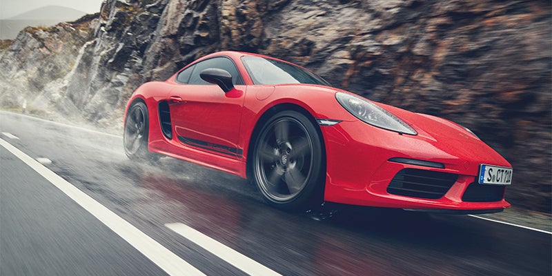 A red sports car on a wet road, spraying water from its spinning tires, with a rocky hillside in the background.
