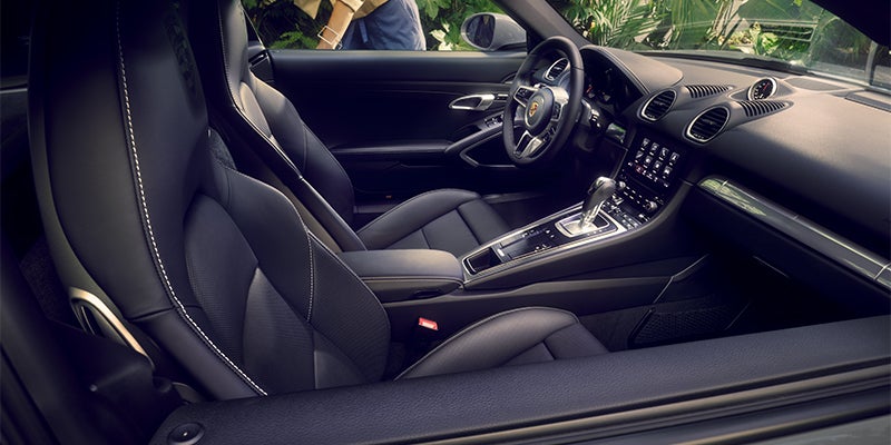 Interior of a parked dark sports car from the driver's side, showing black leather seats and a sleek console.
