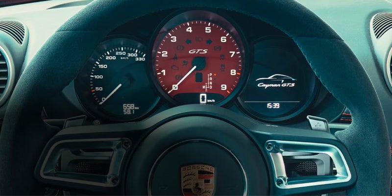The dashboard of a Porsche Cayman GTS, showing the steering wheel, red tachometer, and speedometer.
