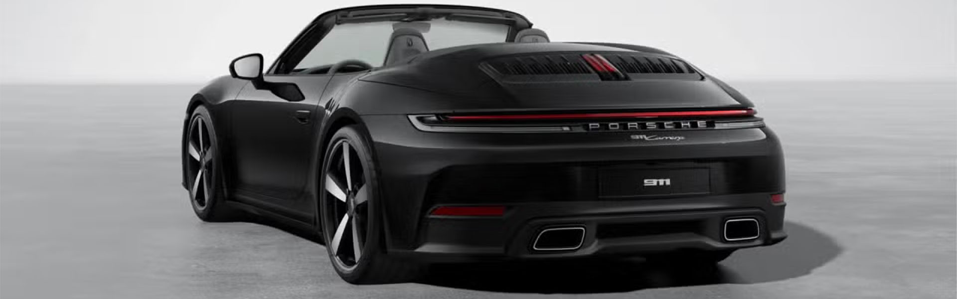Rear three-quarter view of a sleek, dark gray Porsche 911 Carrera convertible with its top down.