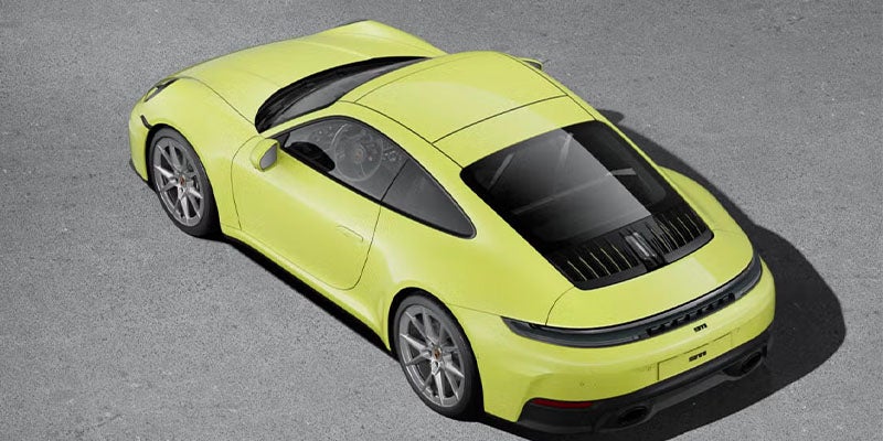 Overhead view of a bright yellow Porsche 911 parked on an asphalt surface, with dark shadows.