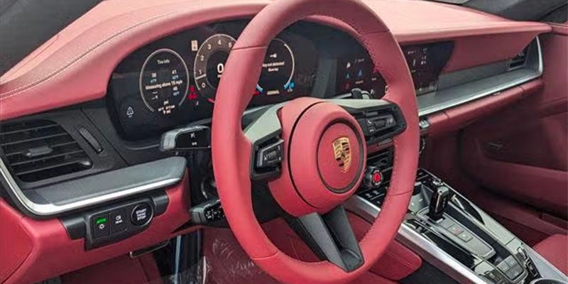 Interior of a modern Porsche sports car with a red leather steering wheel featuring a gold emblem, and a digital dashboard.