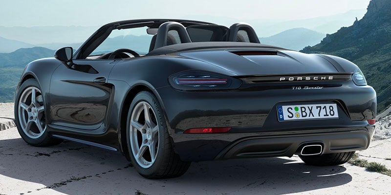 Rear view of a black Porsche 718 Boxster convertible with its top down, rocky landscape in the background.