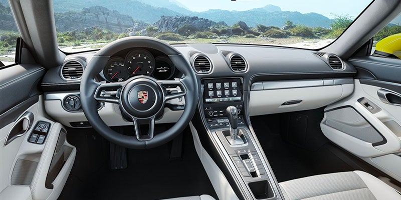 Interior view of an open-top car featuring a black steering wheel, dashboard, and white seats, with mountains in the background.