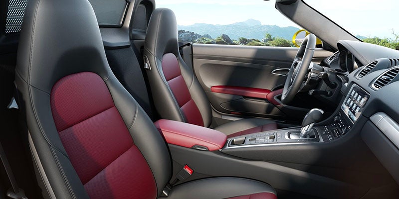 Interior of a sports car with black and red bucket seats, a red armrest, and a mountain landscape in background.