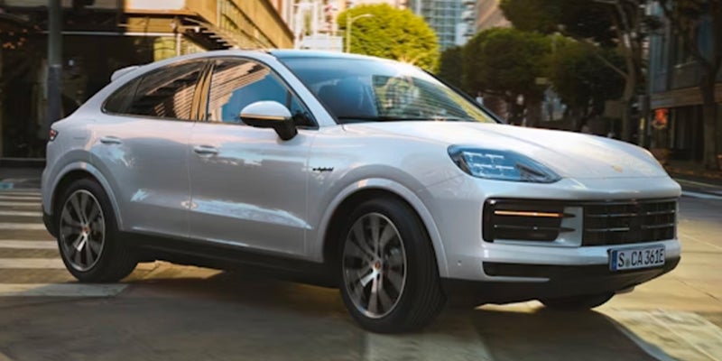 White Porsche Cayenne Coupe, a hybrid SUV, driving on a city street during the day.