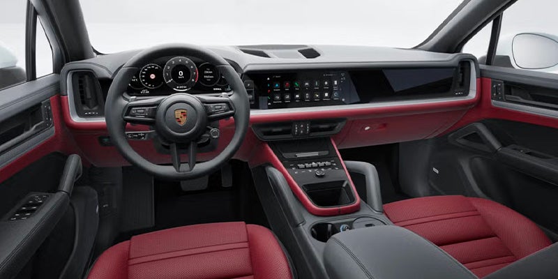 Dark and red interior of a Porsche Cayenne car, showing the dashboard, steering wheel, and seats.