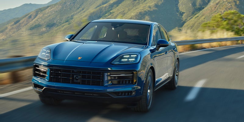 A blue Porsche Cayenne coupe driving on a winding mountainous road.