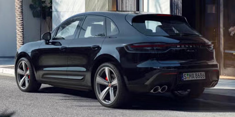 Rear-left view of a shiny black Porsche Macan parked on pavement, with a palm tree in the background.