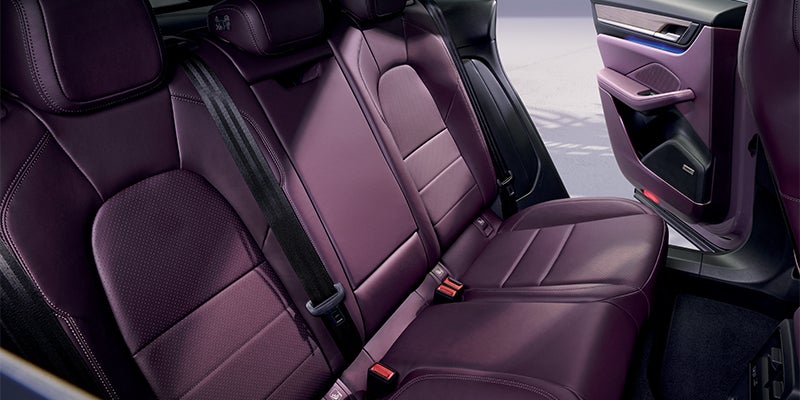 Rear passenger seating of a car, upholstered in deep purple leather with black seatbelts, open door to the right.