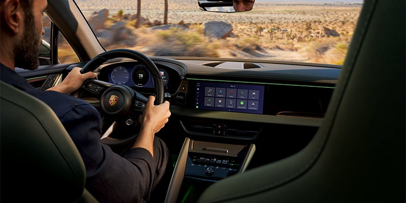 Interior shot of someone driving a Porsche, showing dashboard, steering wheel, and front infotainment display with apps.