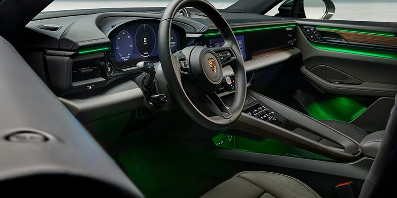 Car interior from the driver's perspective, featuring green ambient lighting on the dashboard, door panels, and floor.