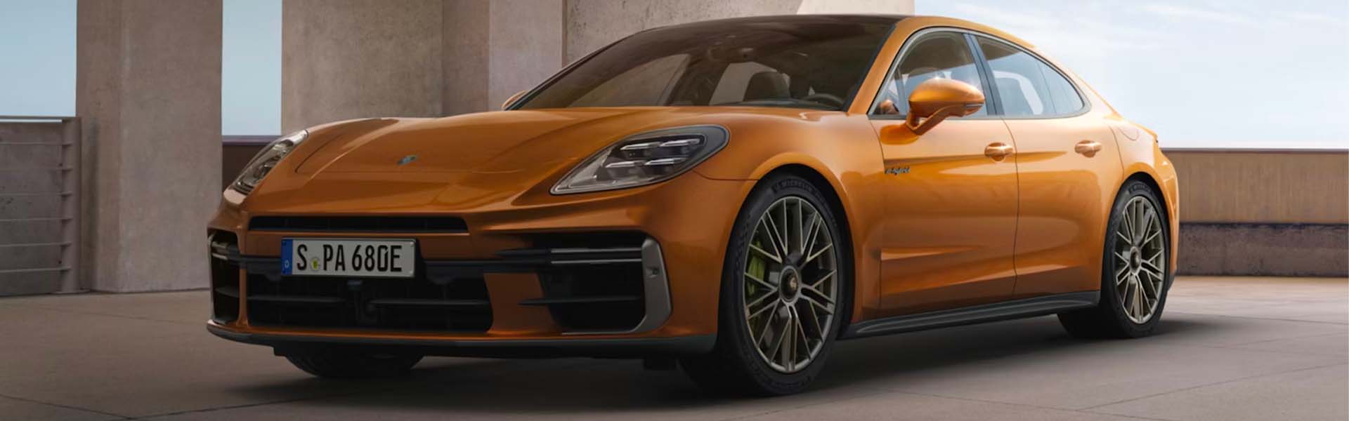 A shiny orange Porsche Panamera, a four-door sports sedan, parked on an outdoor concrete lot.