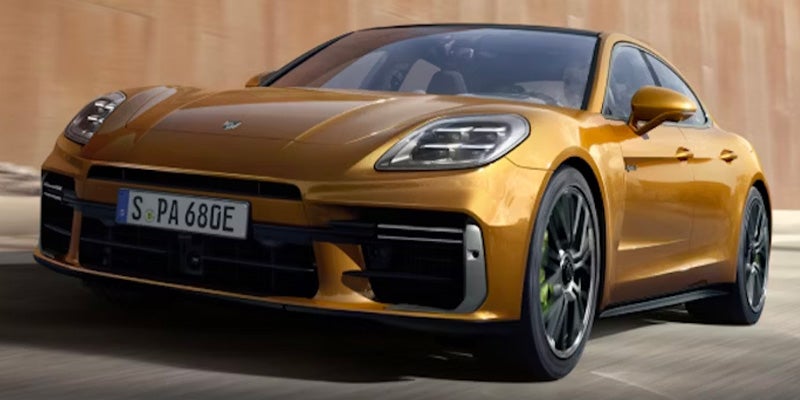 Golden 2024 Porsche Panamera 4 E-Hybrid driving on a road, angled towards the left.