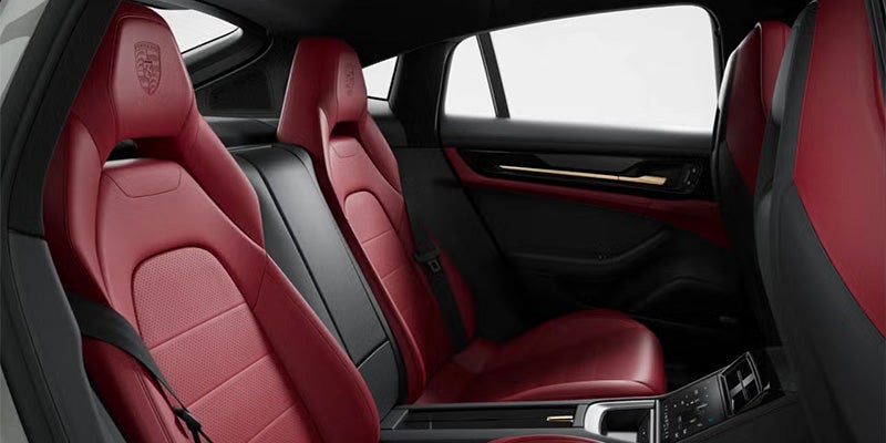 Interior view of a car with two rows of red and black leather seats, and a black-paneled door with gold trim.