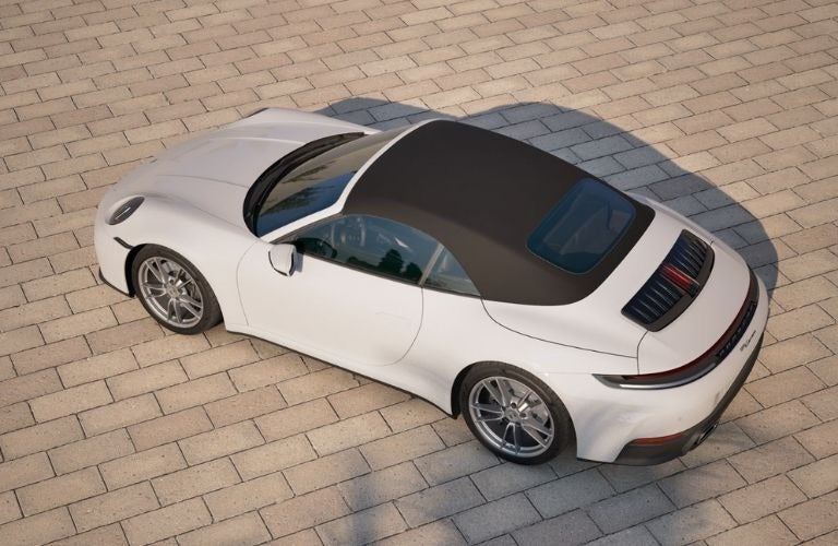 Overhead view of a white Porsche 911 Targa with a black convertible top, parked on light gray paver stones.