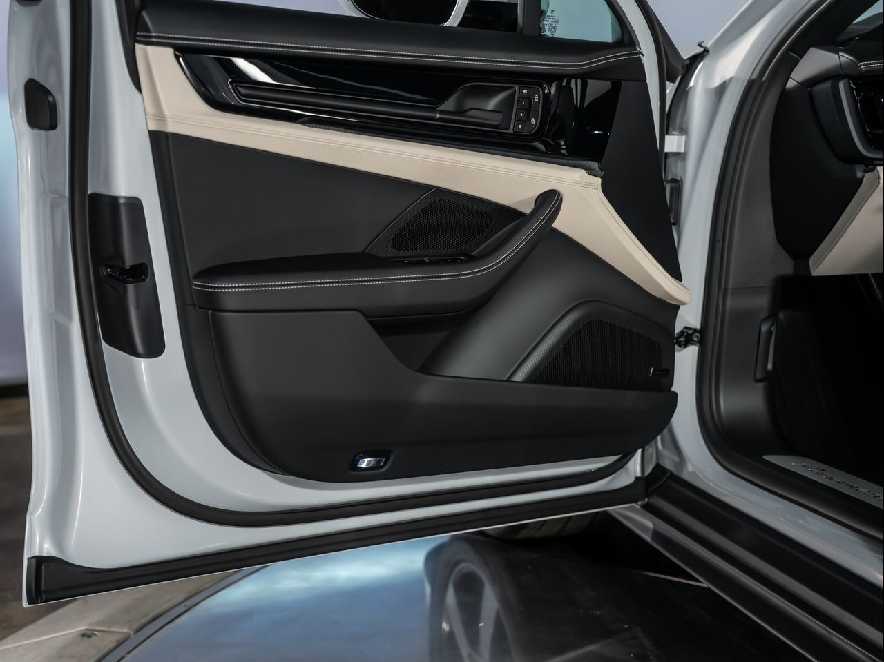 Open driver's side car door, revealing a black and tan interior panel with sleek design and white stitching.