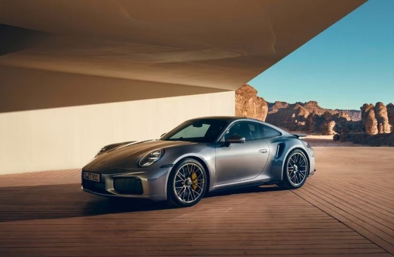 Silver Porsche 911 GT2 RS parked on a wooden deck next to a white wall, desert mountains in the background.