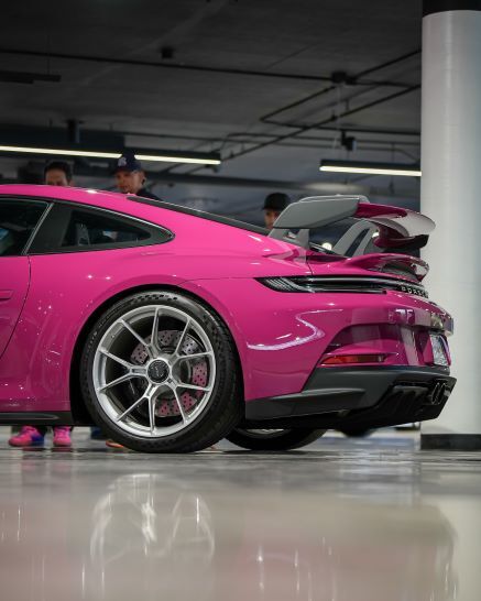 Rear view of a bright pink Porsche sports car with a large spoiler and silver wheels, in a garage.