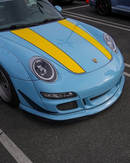 Light blue Porsche with two yellow racing stripes centered on the hood.
