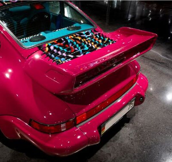 Rear view of a fuchsia pink sports car with a vibrant, multicolored checkered engine cover and large spoiler.
