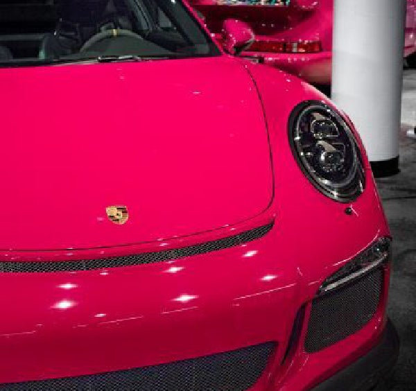 A close-up of the front and right side of a shiny hot pink Porsche against a blurry dark background.