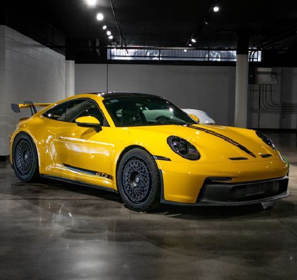 A bright yellow Porsche 911 GT3 with a black racing stripe and black wheels is parked in a showroom.