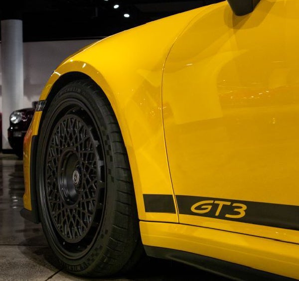 Close-up of a bright yellow Porsche GT3 showing the black multi-spoked wheel and GT3 decal.