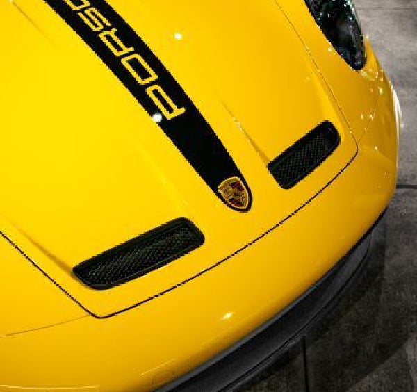 Close-up of a bright yellow Porsche car hood with a black stripe and PORSCHE text written on it.