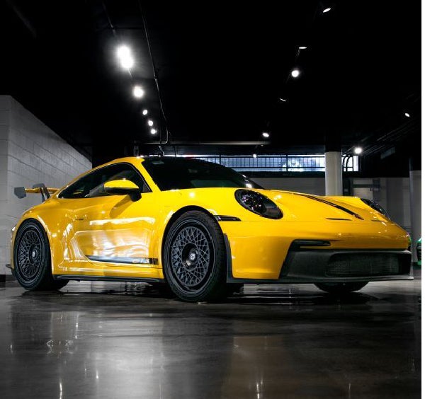 Bright yellow Porsche 911 GT3 with black racing stripes and aero kit, parked on a reflective garage floor.