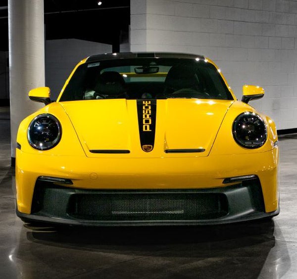 Front view of a bright yellow Porsche sports car with a black stripe and PORSCHE text on its hood.