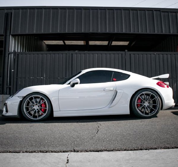 Side view of a white Porsche sports car with black rims and red brake calipers, parked against a dark building.