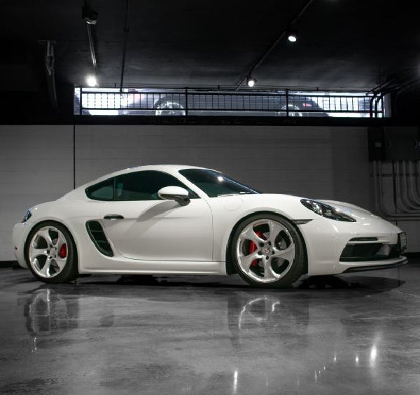 Brightly lit side view of a white Porsche 718 Cayman GT4.