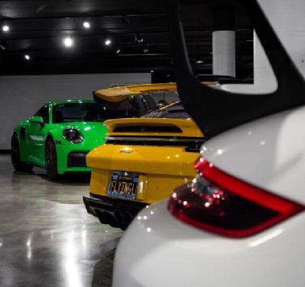 A white car's spoiler and taillight in the foreground, with yellow and green sports cars extending into the background.