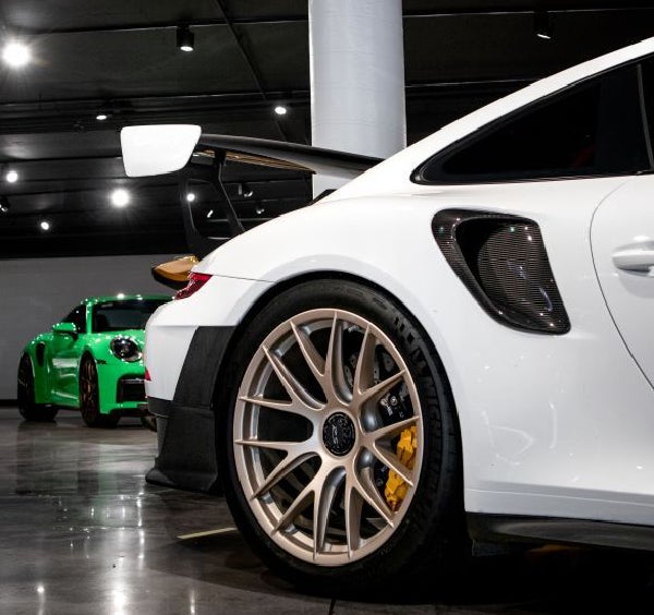 Rear quarter view of a white Porsche 911 GT2 RS with bronze wheels and yellow brake calipers; green Porsche behind.
