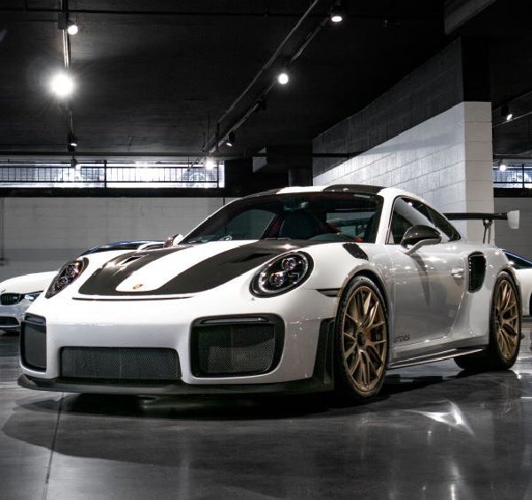 A white Porsche 911 GT2 RS with a black stripe, gold wheels, and a rear spoiler in a showroom.