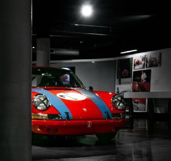 A red race car with blue stripes and cross-taped headlights, displayed in a dark, glossy room.