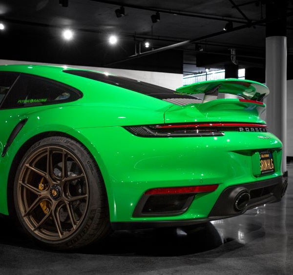 Rear view of a bright green Porsche 911 GT3 with a large spoiler and bronze wheels, parked indoors.