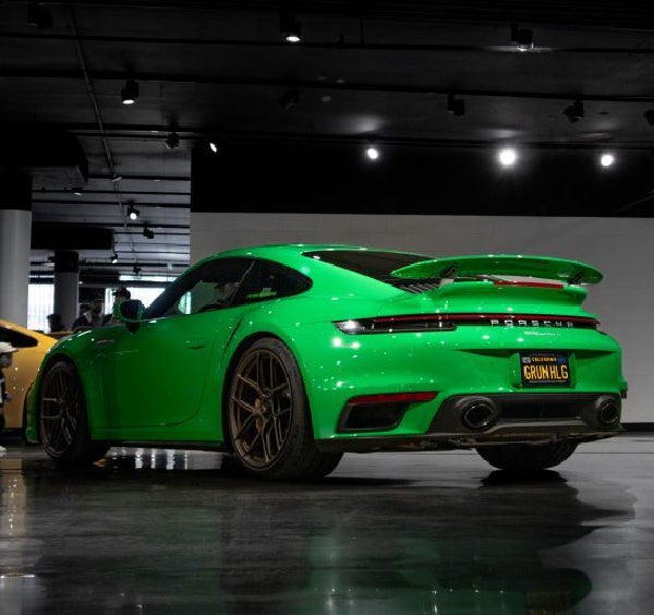 Rear view of a bright green Porsche 911 GT3 with a custom license plate GRUN
HLG in a dark showroom.