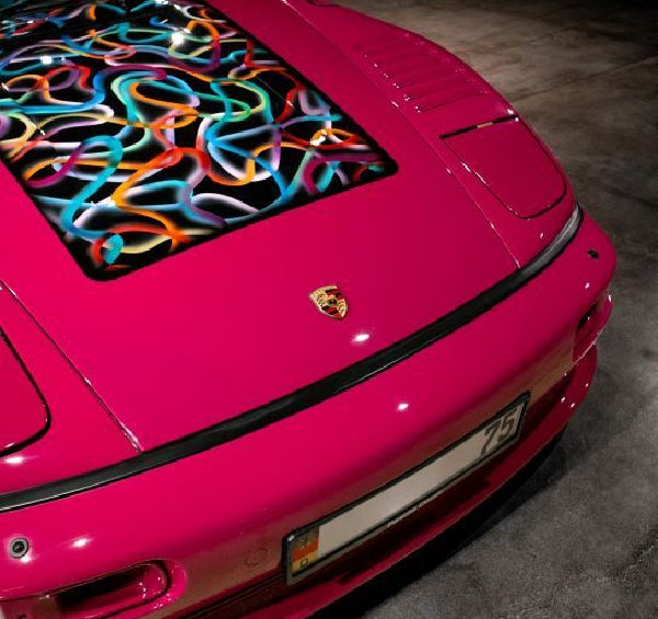 A vibrant pink Porsche with a colorful, abstract swirl pattern on its front hood.