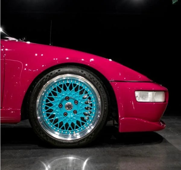 Close-up of the front right quarter of a bright pink car with a vibrant teal spoked wheel.